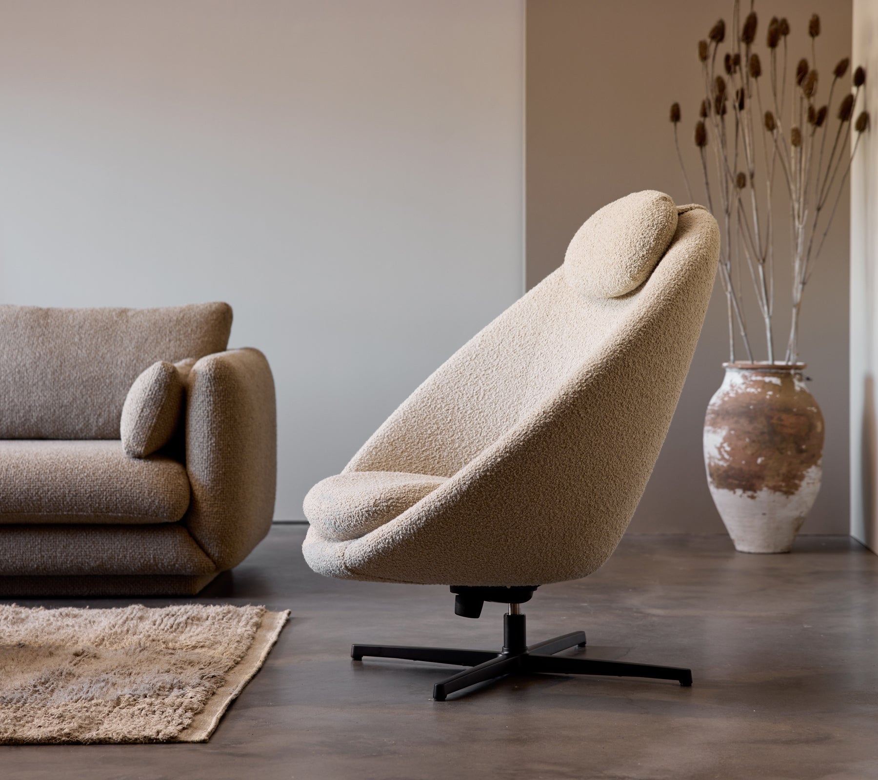 Pace chair in taupe fabric next to a Bloom 3-seater sofa, complemented by a decorative vase and subtle floor texture.