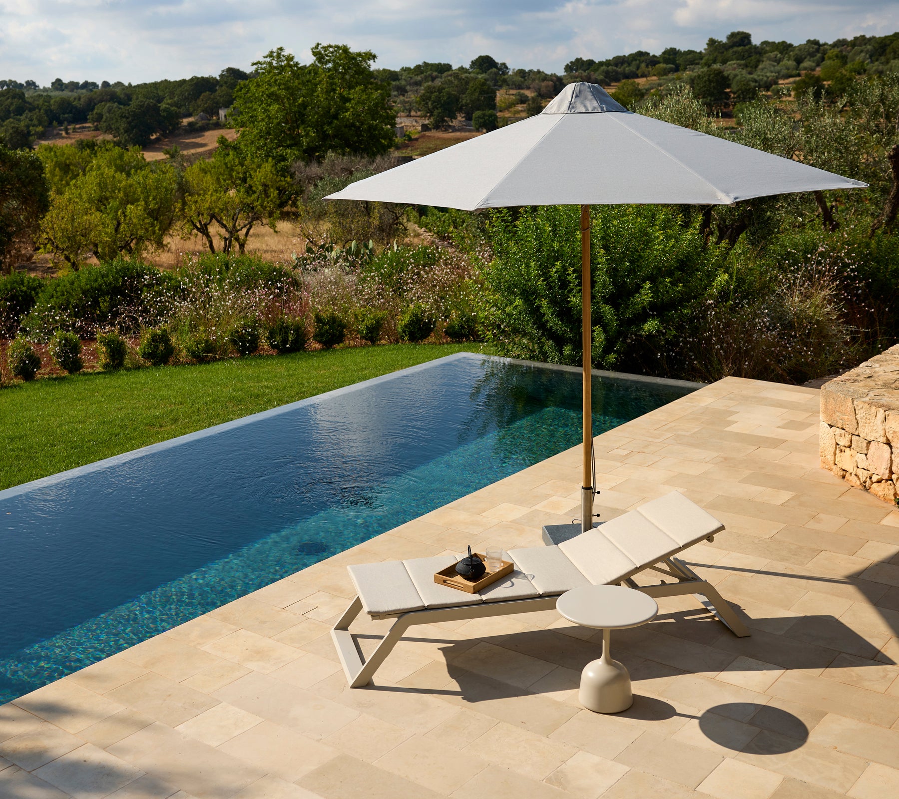 Modern outdoor lounge area featuring a white chair, umbrella, and side table by a pool.