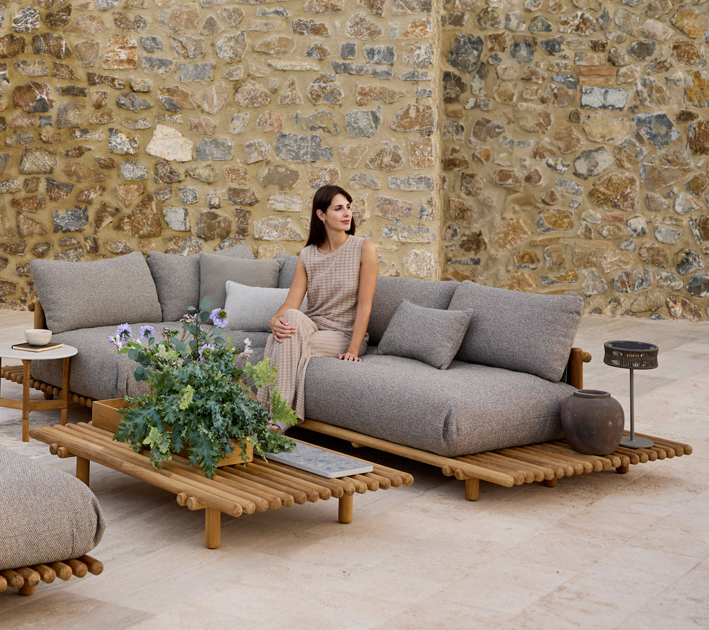 A stylish corner sofa with cushions, accompanied by a matching coffee table, set against a textured stone wall.