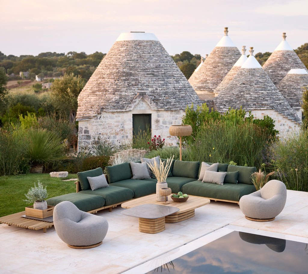 Modern outdoor lounge area with green sectional sofa, grey armchairs, and wooden coffee table.