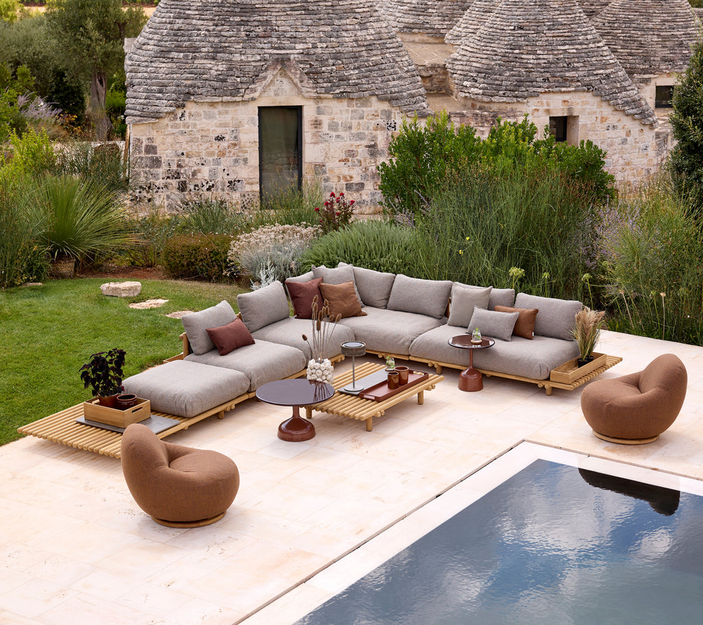 Modern grey sectional sofa with brown lounge chairs beside a pool in a minimalist setting.