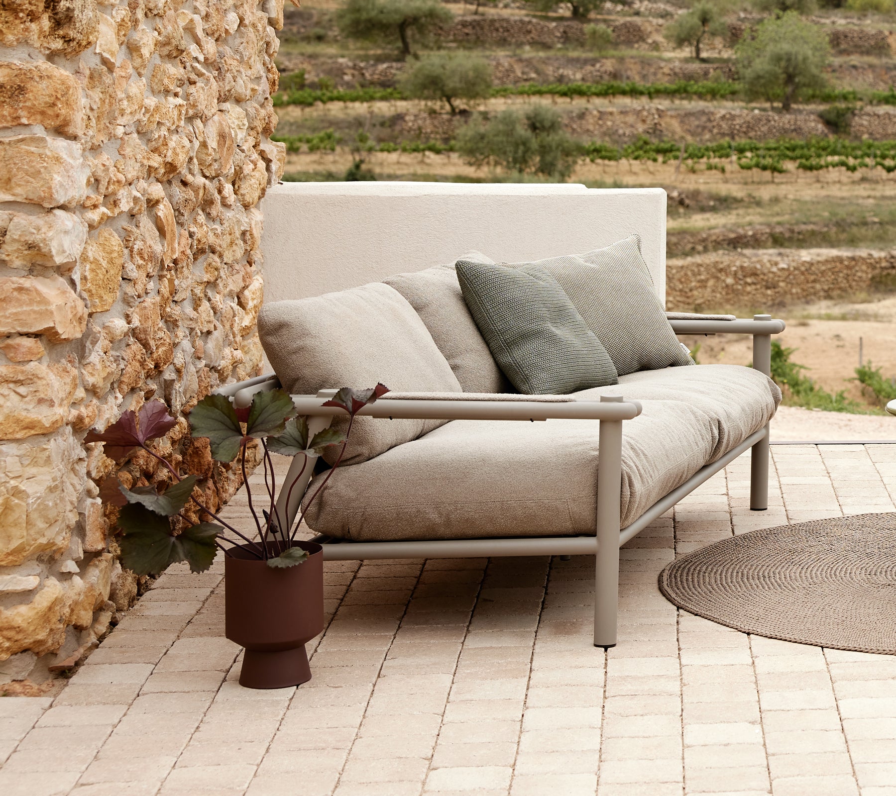 A modern sofa with soft cushions and an aluminum frame, accompanied by a potted plant on a patterned tile surface.