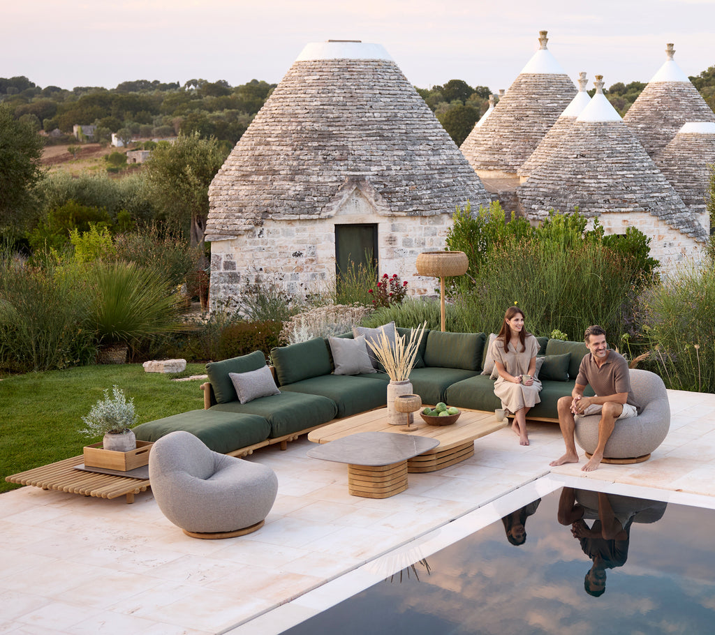 Modern outdoor lounge area featuring a green sofa, grey chair, and round coffee table.