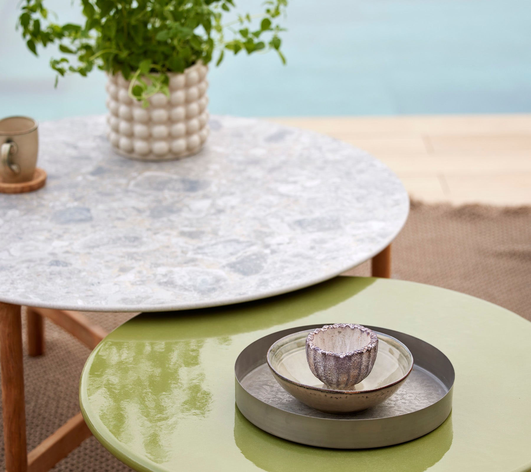 A Twist multi-colour table with a glazed lava stone top, accompanied by a decorative bowl and plant in a stylish setting.