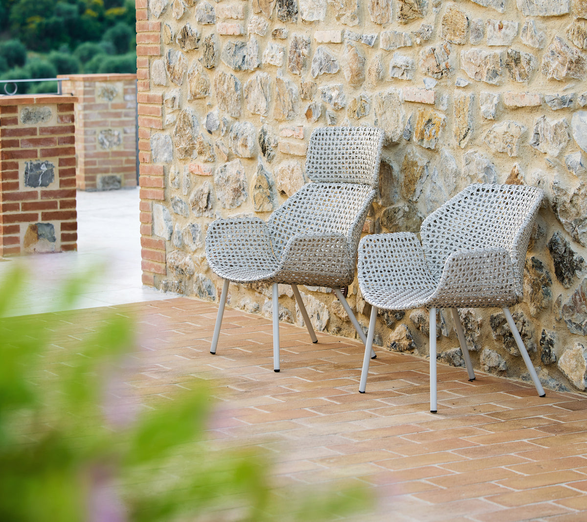 Two Vibe highback lounge chairs in dark sand, stylishly designed, set against a textured stone wall with a warm, inviting atmosphere.