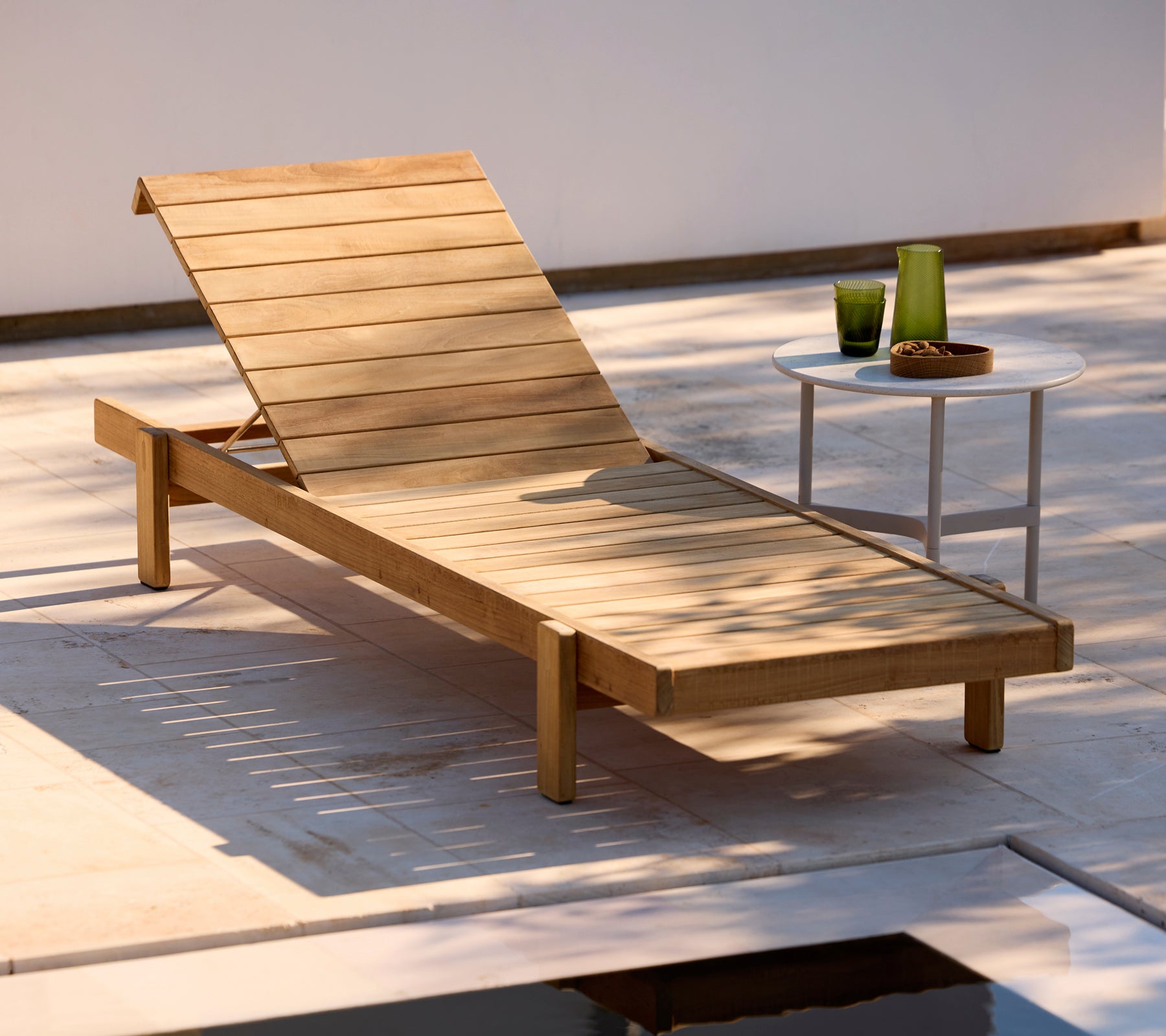 Wooden lounger with a white side table in a modern outdoor setting.