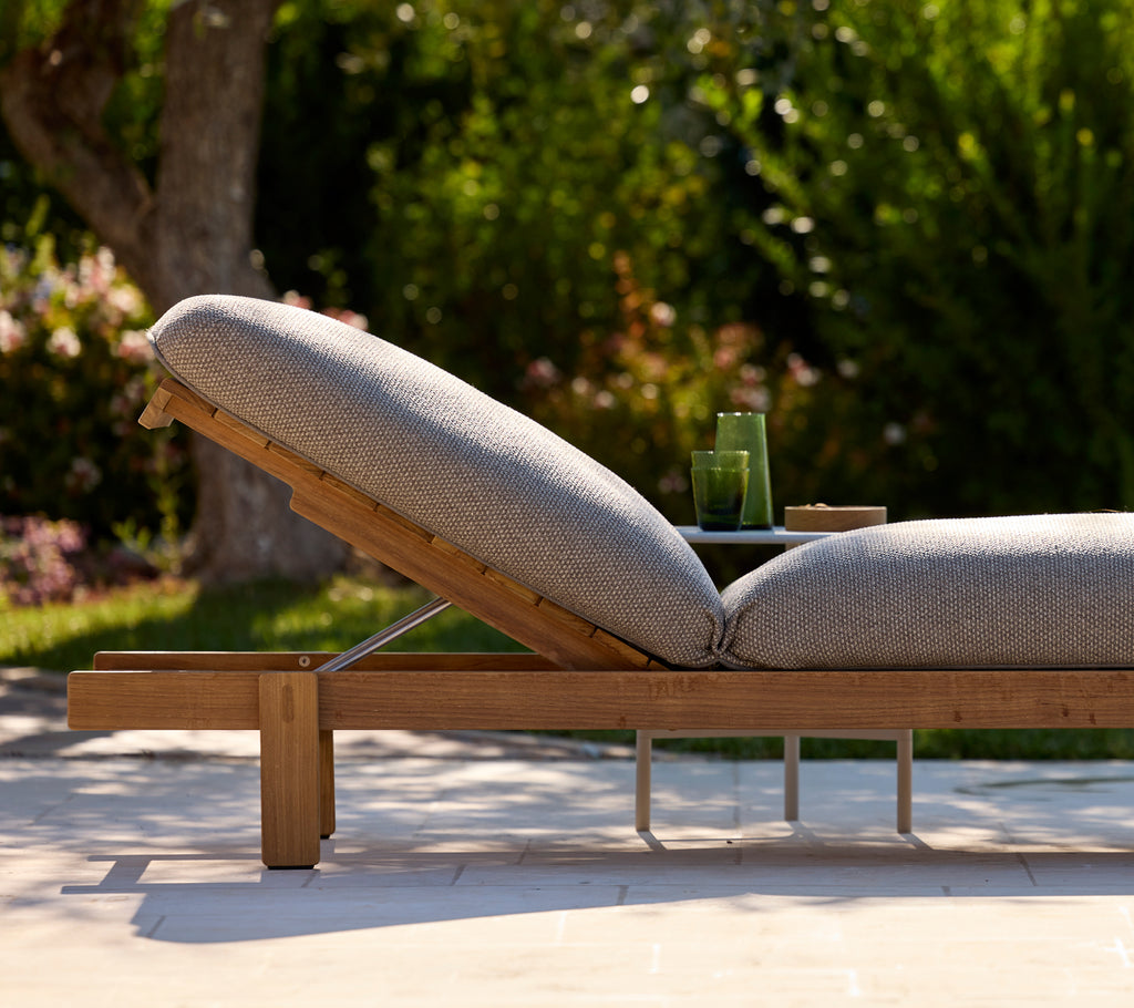 Modern grey lounge chair with side table in a lush outdoor setting.