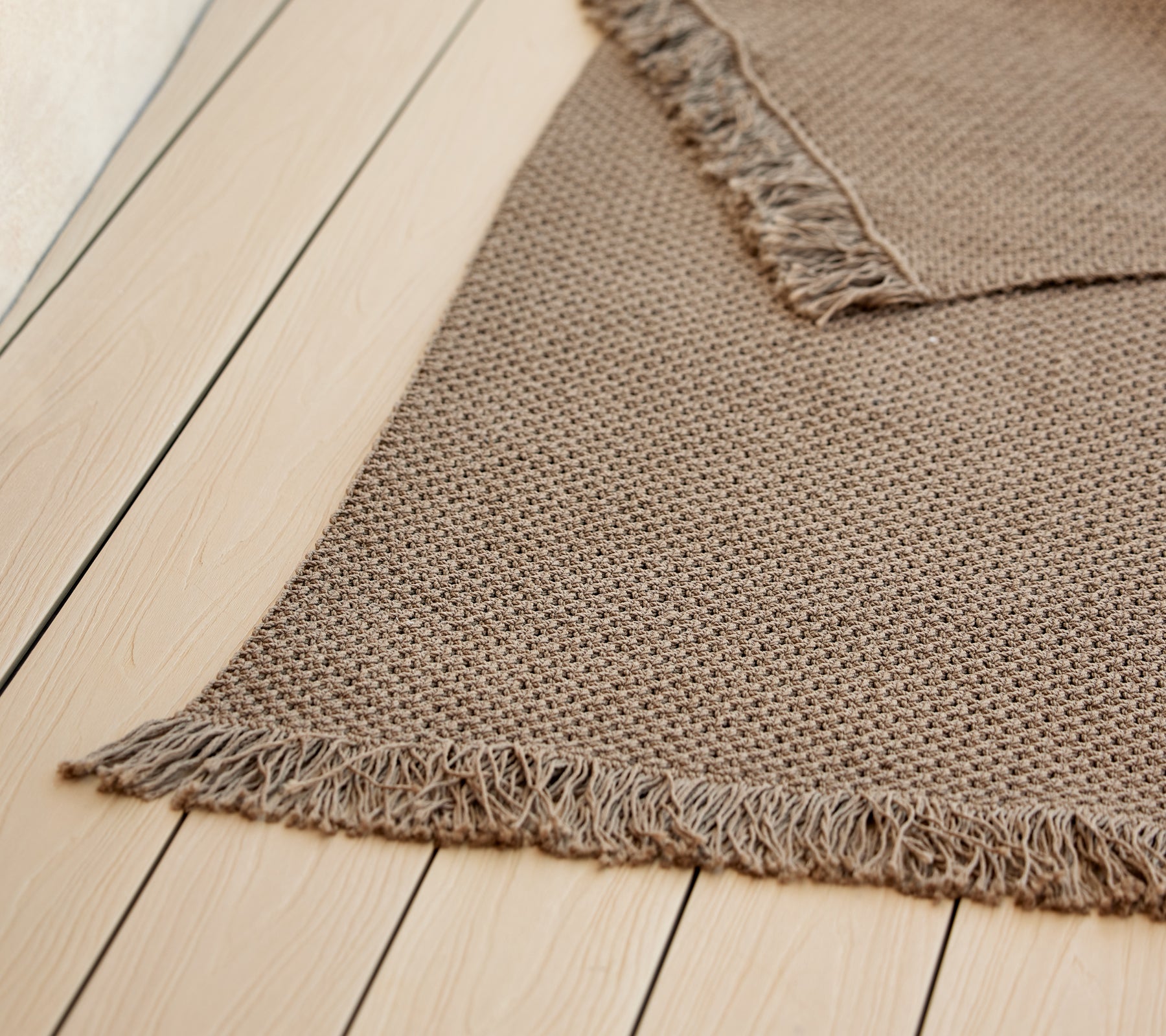 A textured knit rug with fringed edges, showcasing a warm, neutral color, enhancing its cozy aesthetic.